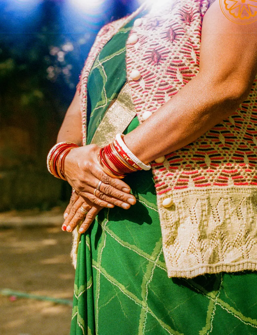 Woman wearing traditional green and red patterned clothing and red bangles.